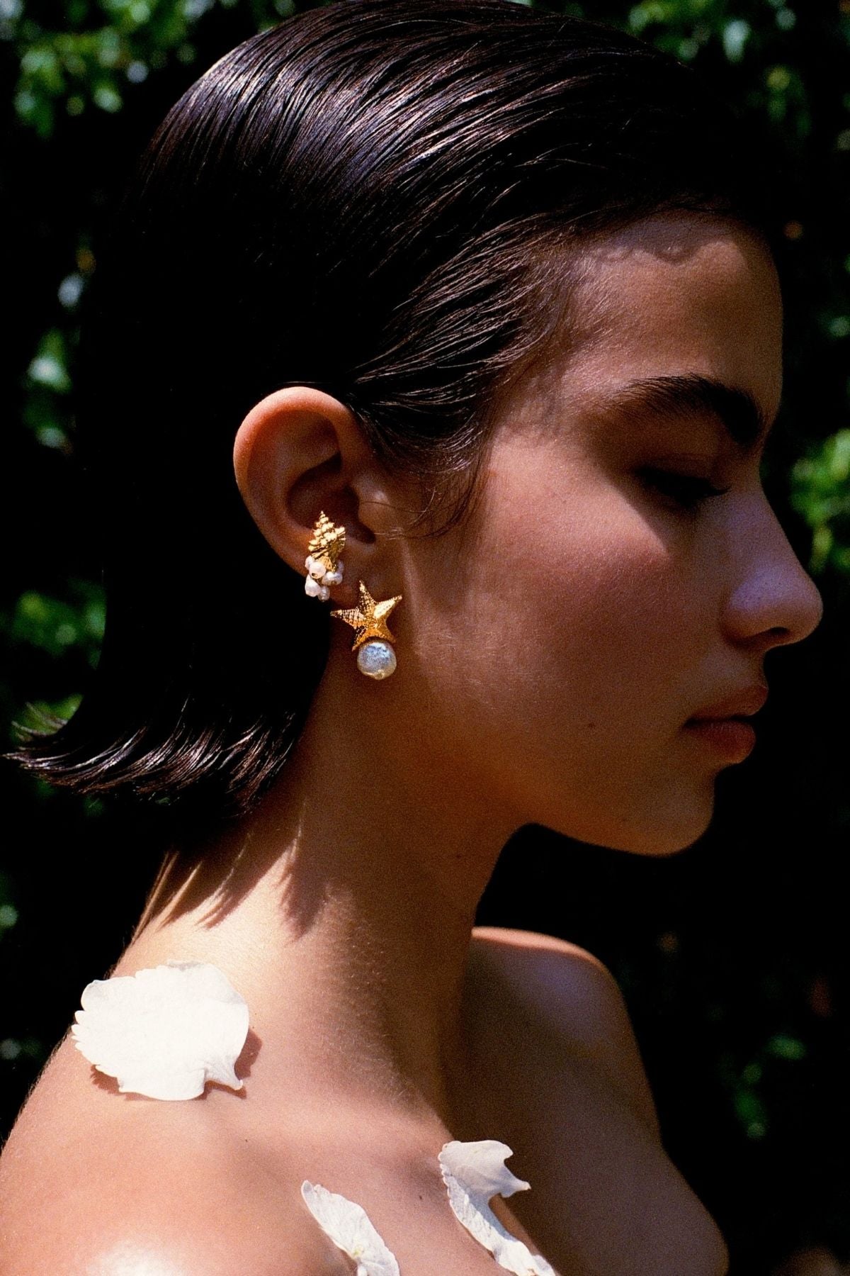Close-up of a person wearing gold earrings with a blurred green background