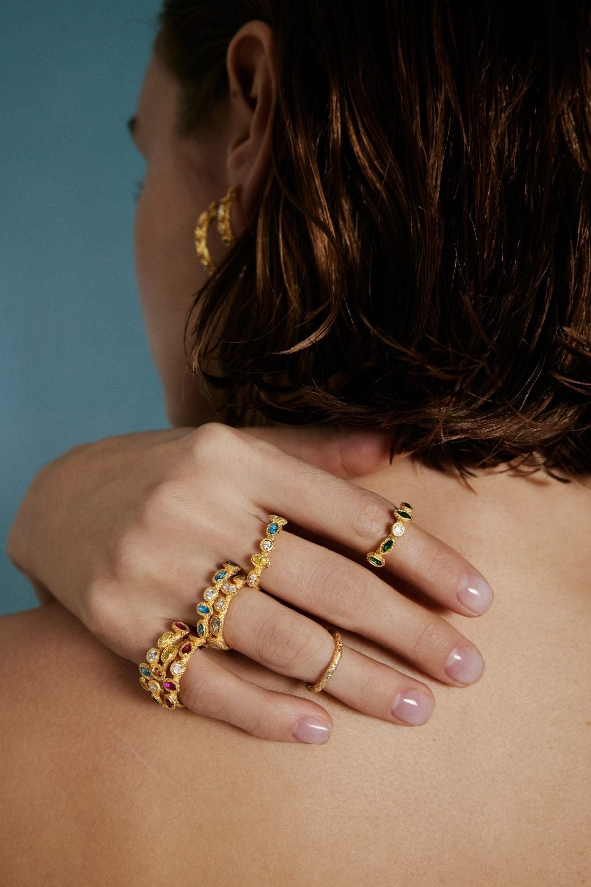 Close-up of a person wearing multiple gold rings with gemstones on a blurred background