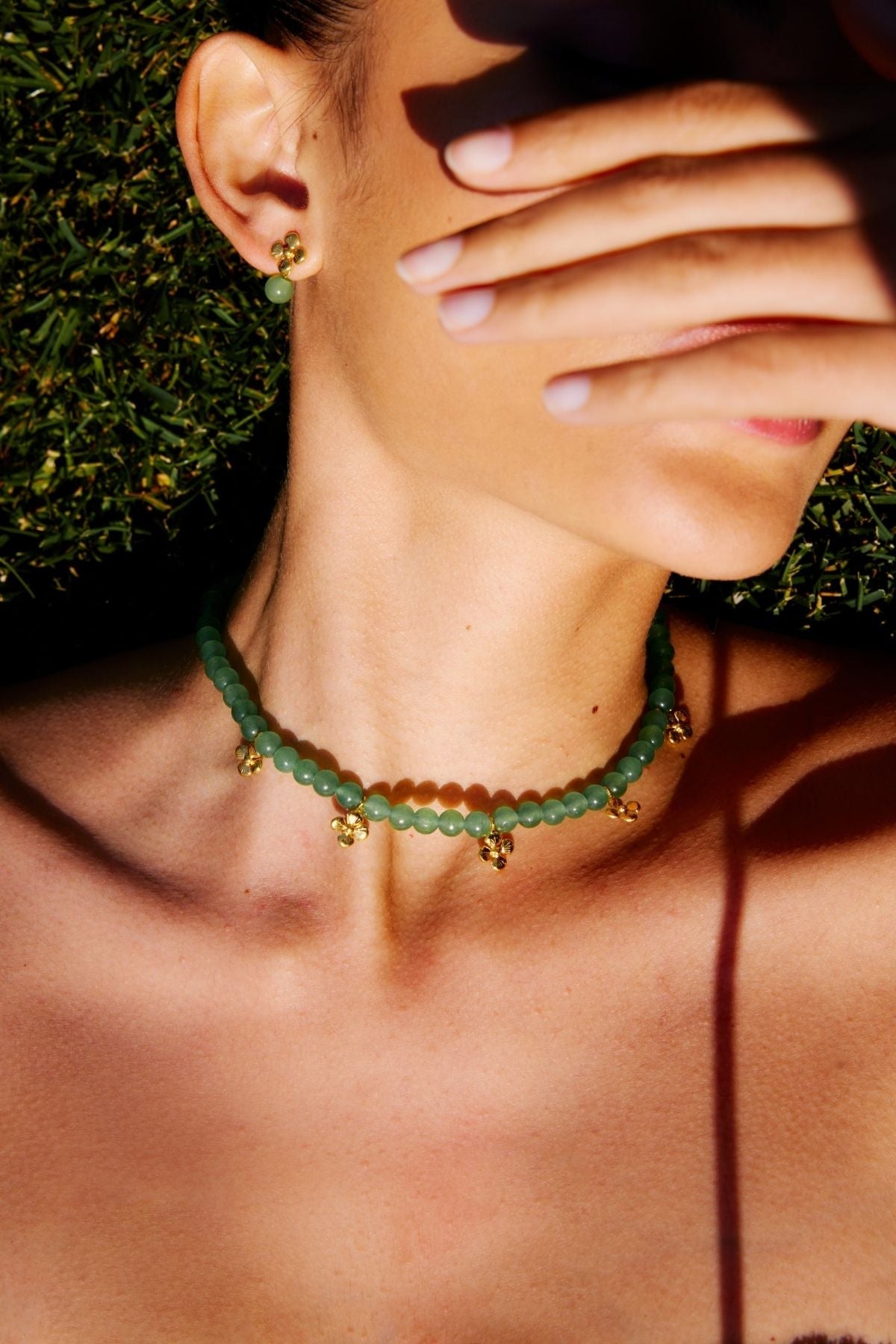 Close-up of a person wearing a green beaded necklace with gold accents, set against a natural background.