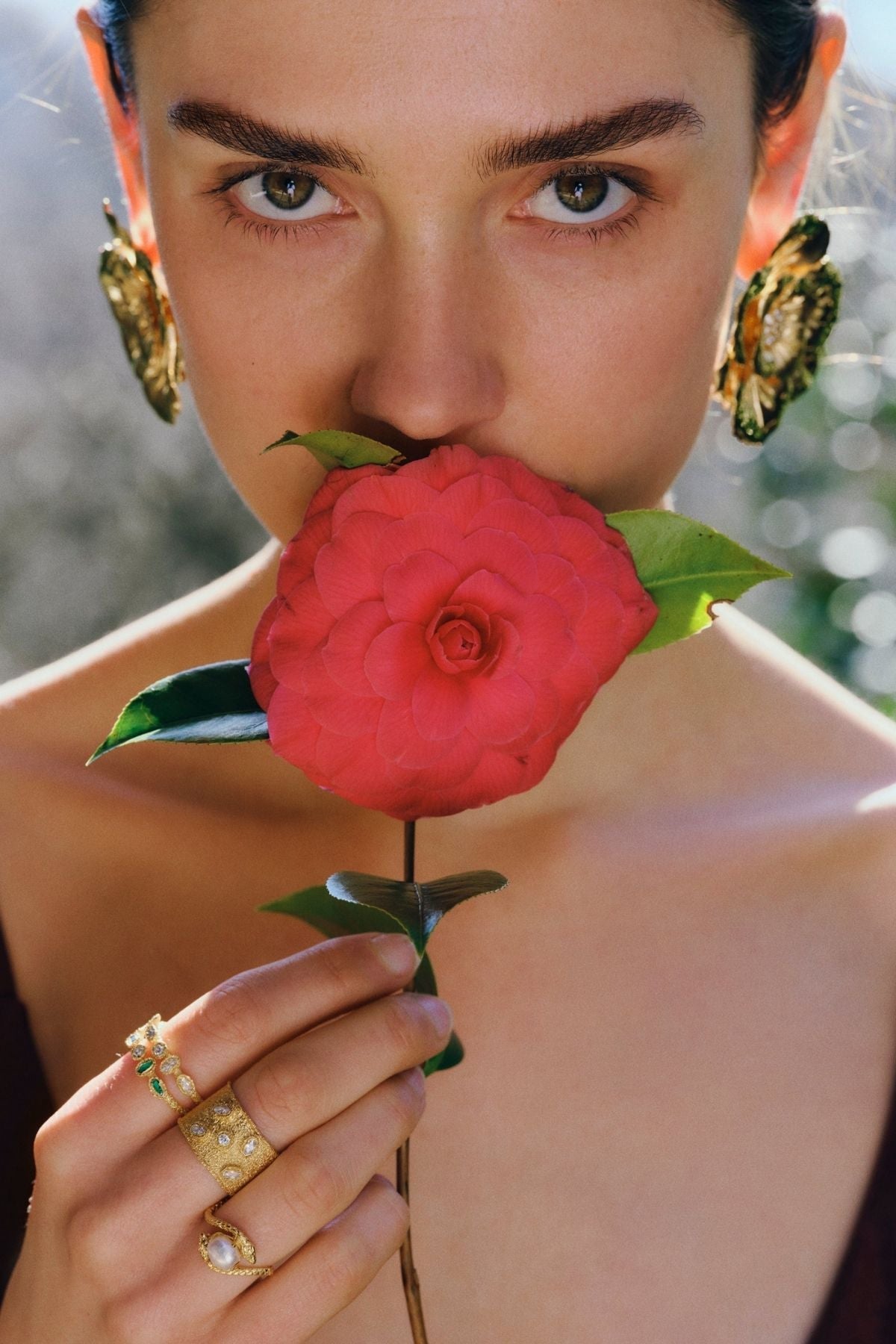 Person holding a red flower to their nose with a blurred natural background