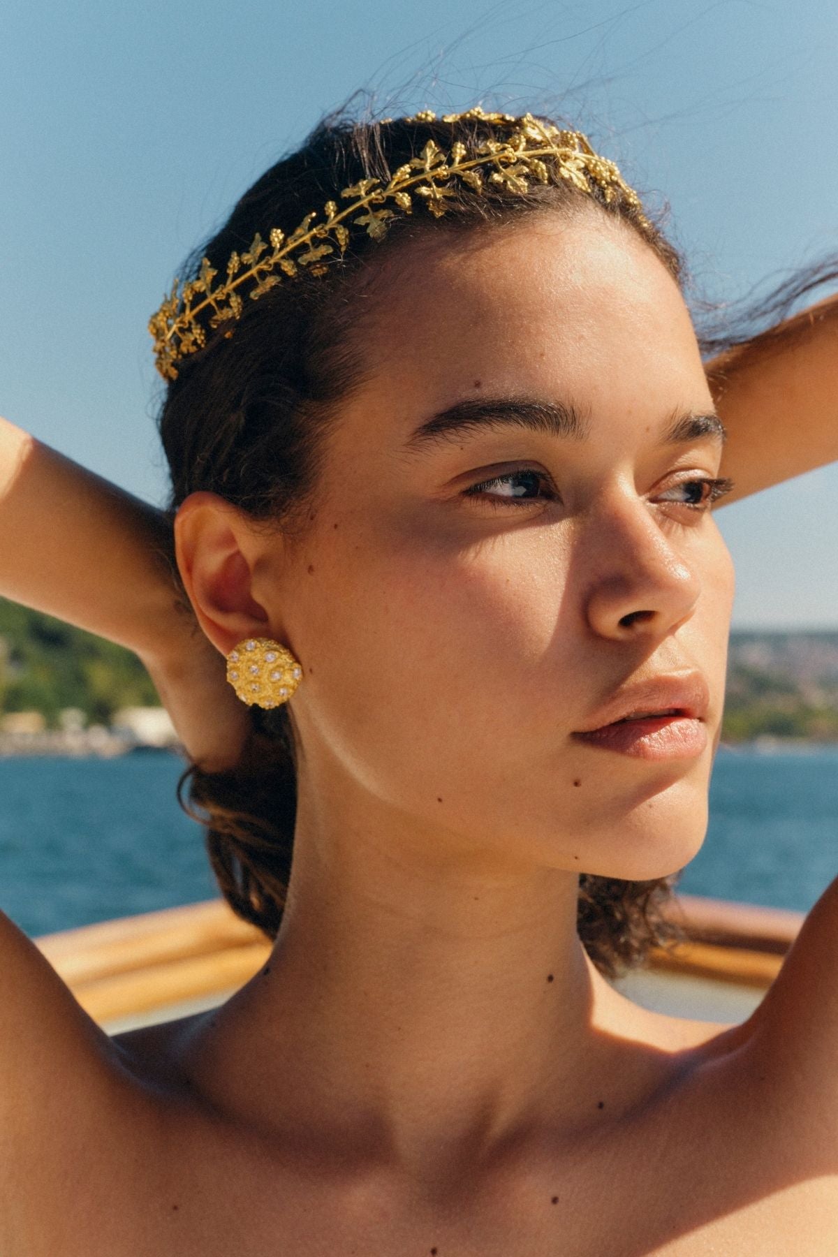 Woman wearing a gold headband and earrings with a scenic background