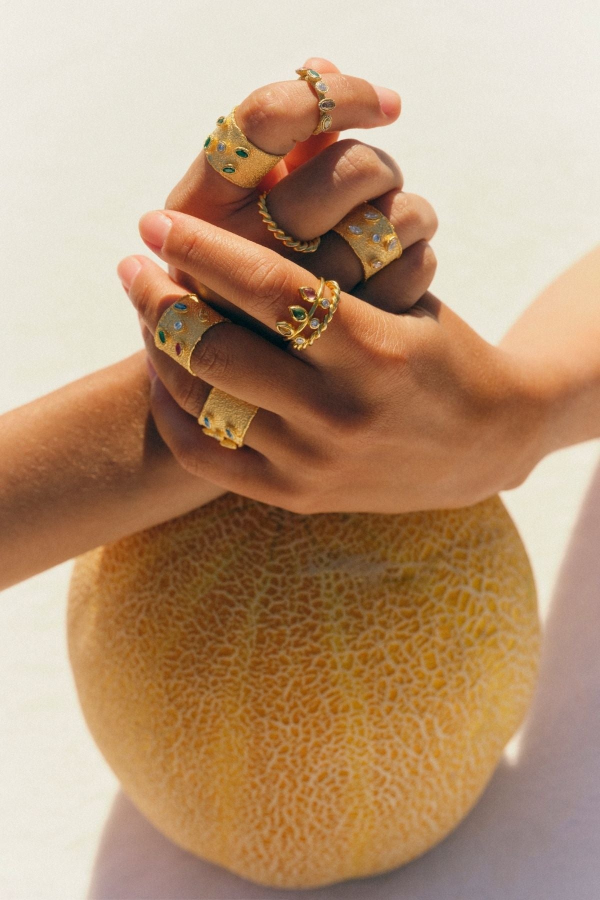 Hands with gold rings holding a cantaloupe against a light background