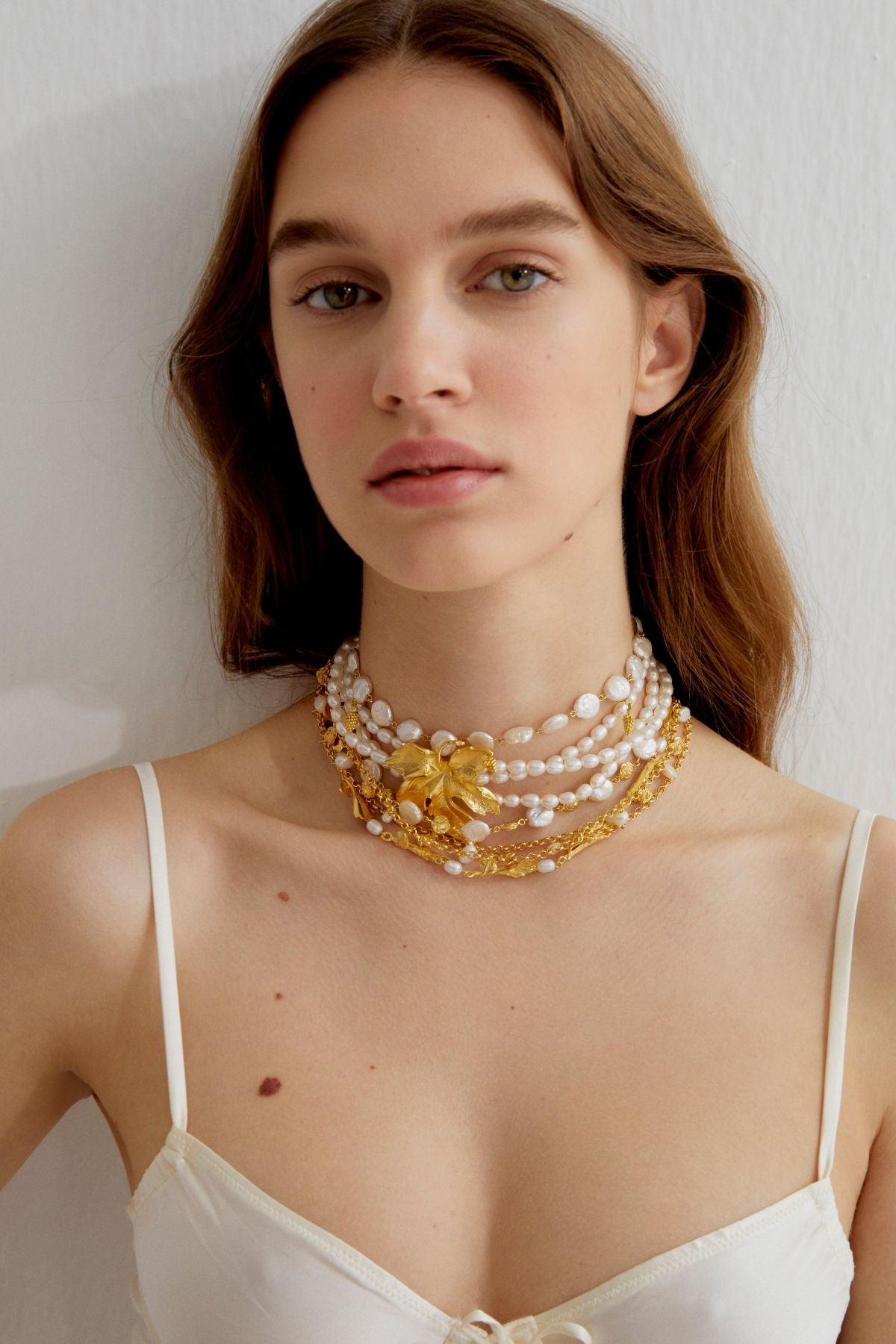 Woman wearing a stack of gold and pearl necklaces against a plain background