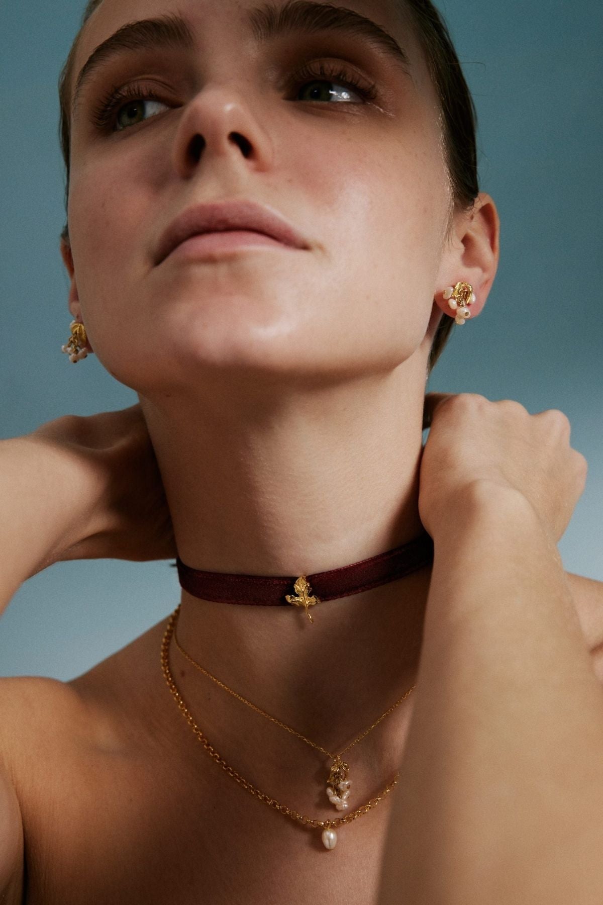 Close-up of a person wearing gold necklaces and earrings against a blue background