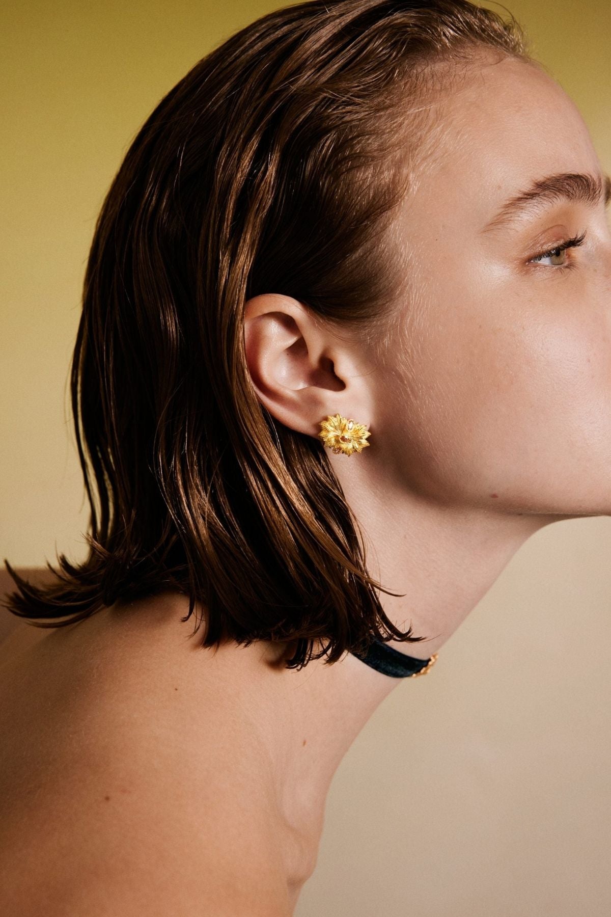 Close-up of a person wearing gold earrings with a neutral background