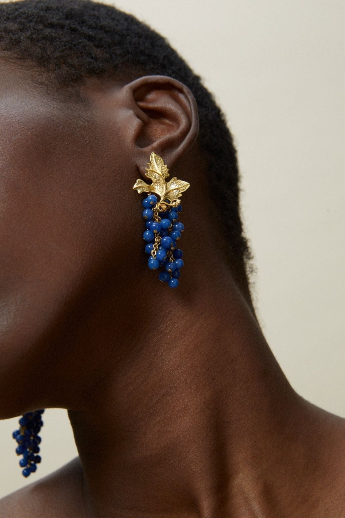 Close-up of a person wearing blue beaded earrings with gold accents.