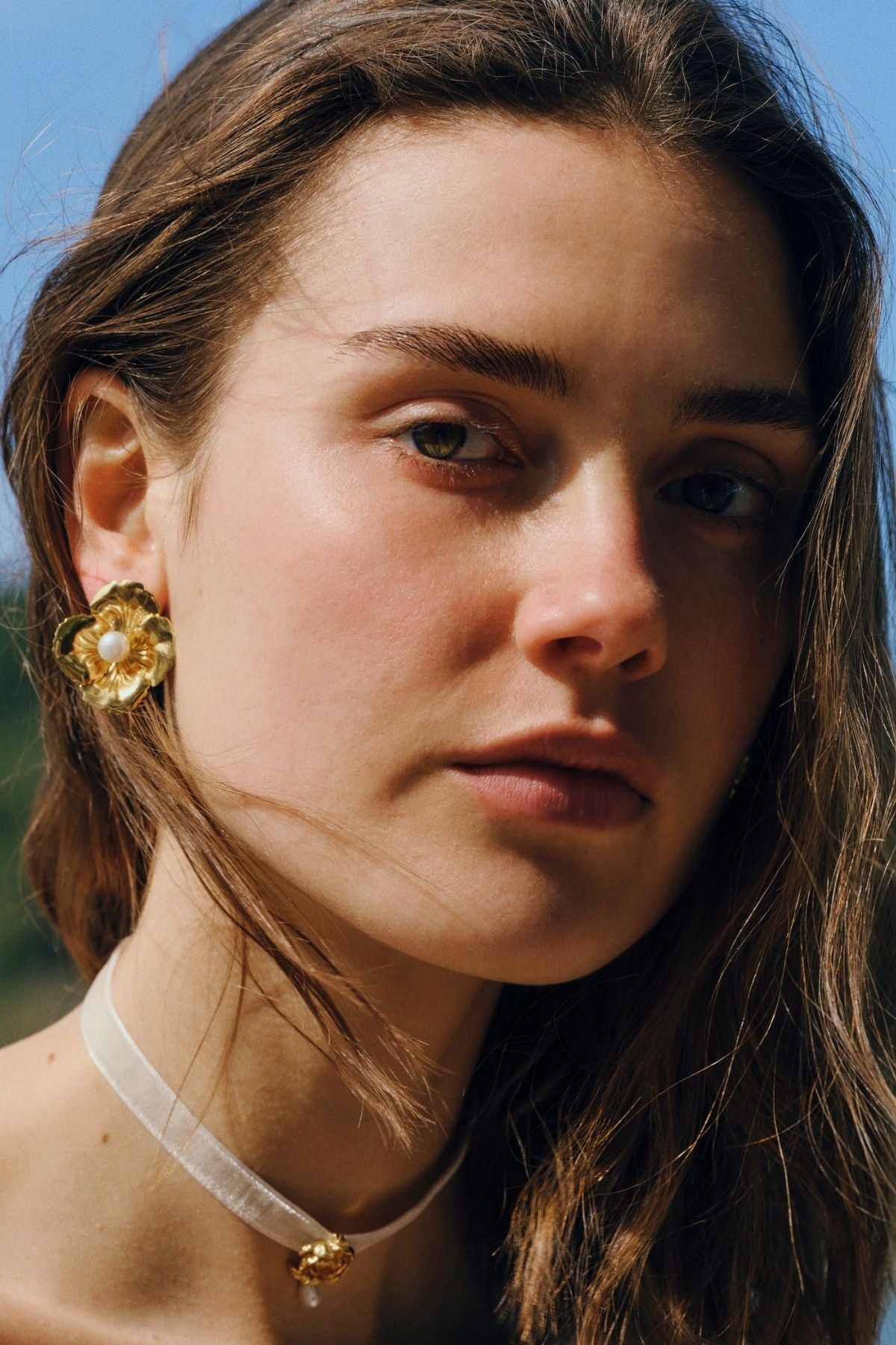 Close-up of a person wearing gold earrings with a blurred natural background