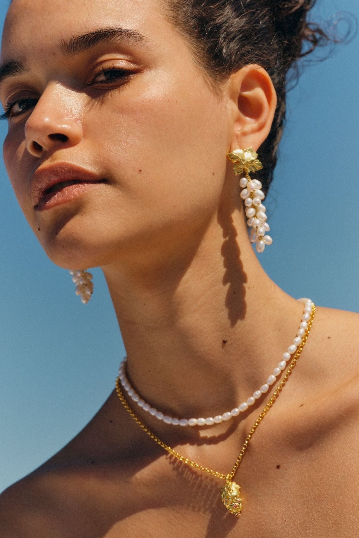 Woman wearing pearl and gold jewelry against a clear blue sky