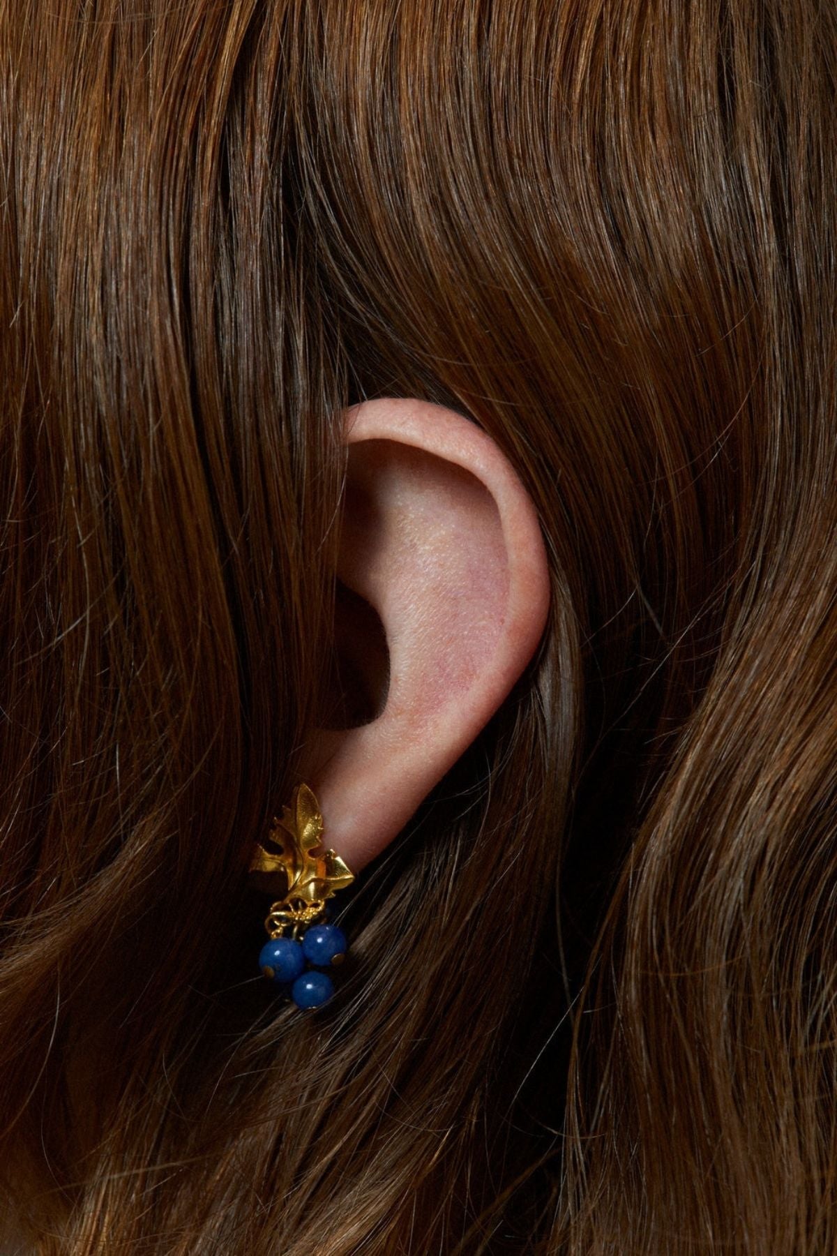 Close-up of an ear wearing a gold and blue earring with brown hair.