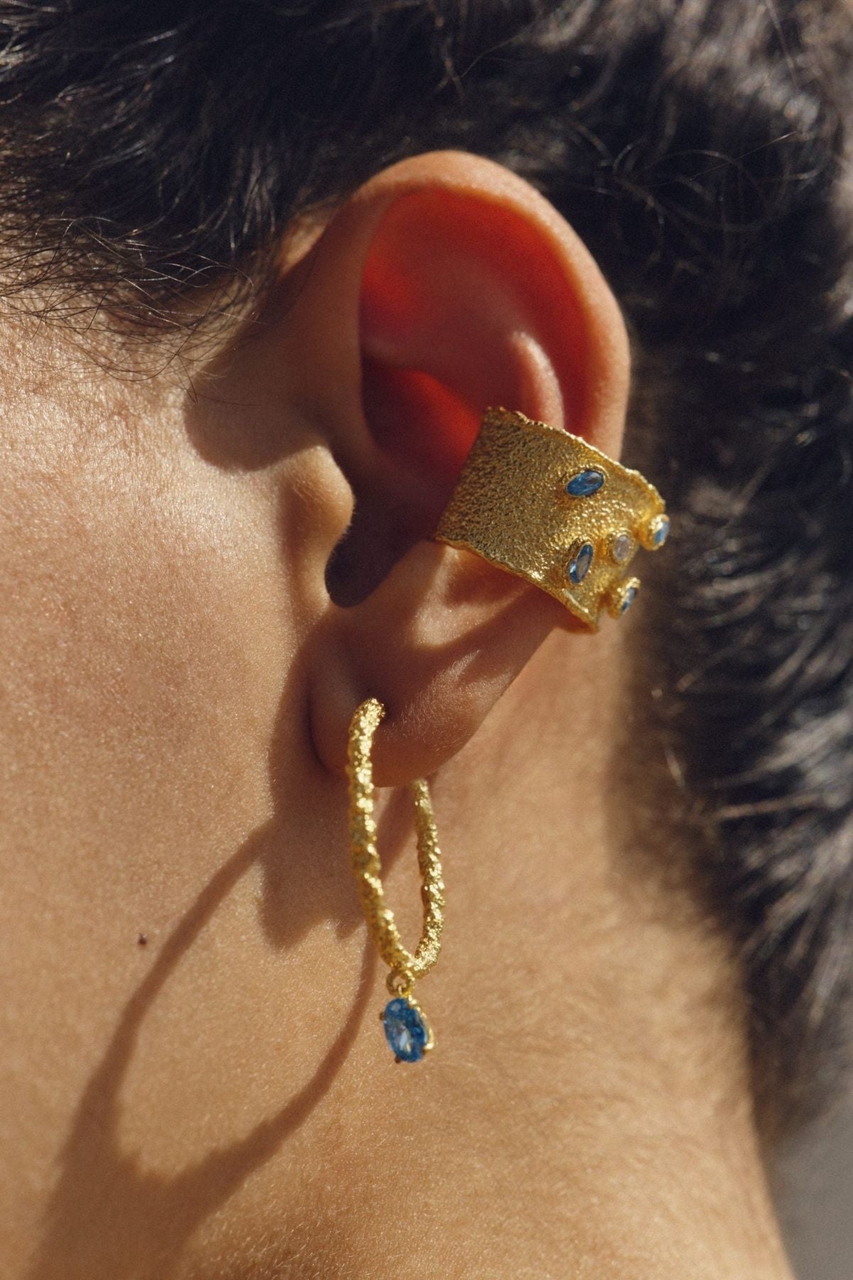 Gold earrings with blue gemstones worn by a person