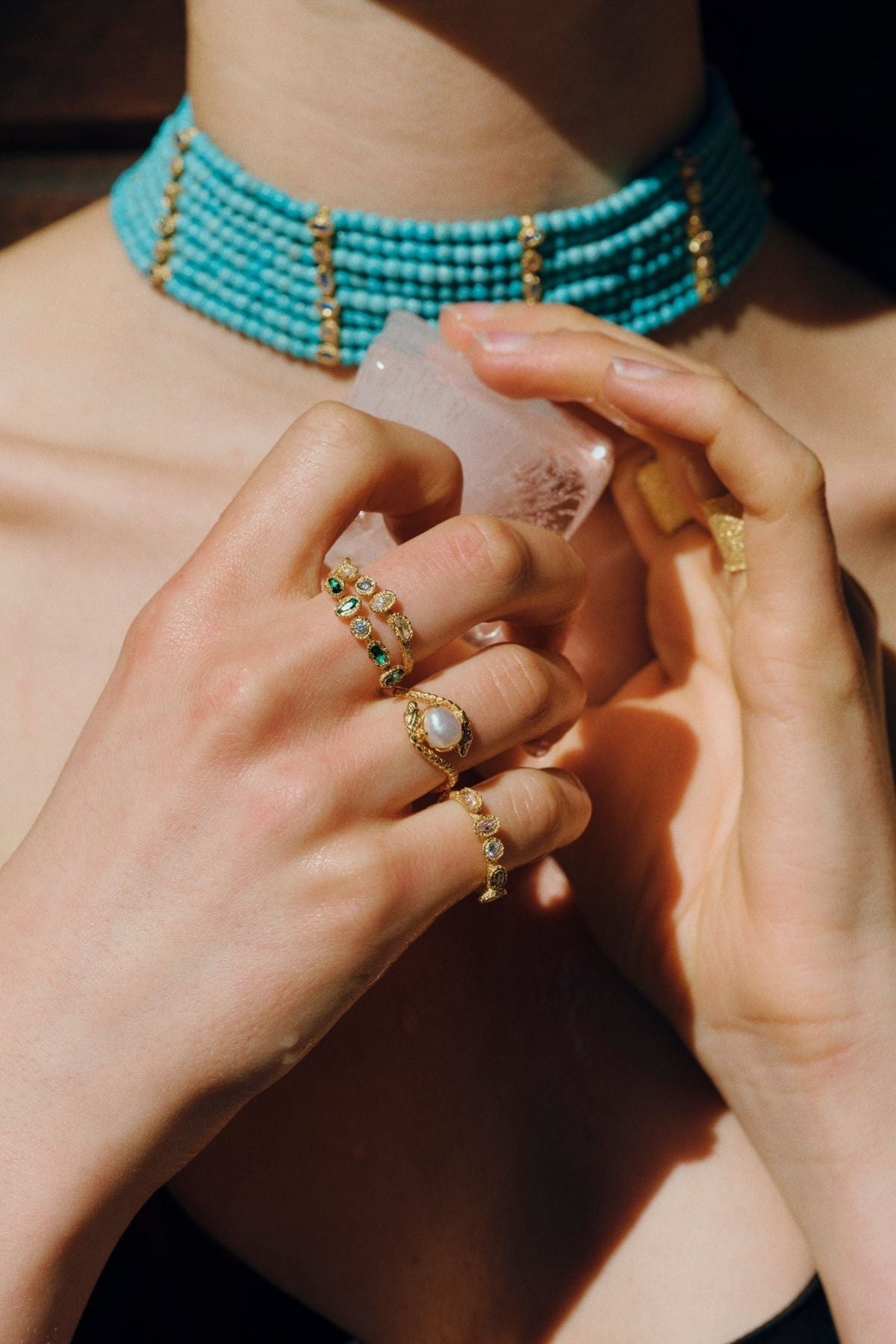 Person wearing a turquoise beaded choker and gold jewelry holding a clear bottle.