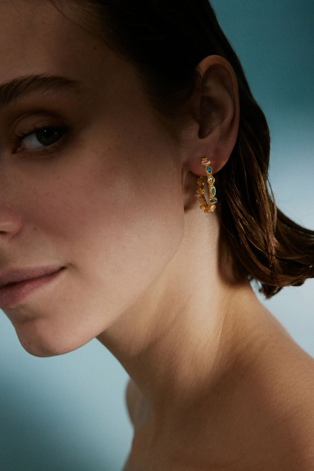 Close-up of a person wearing gold earrings with gemstones against a blurred background