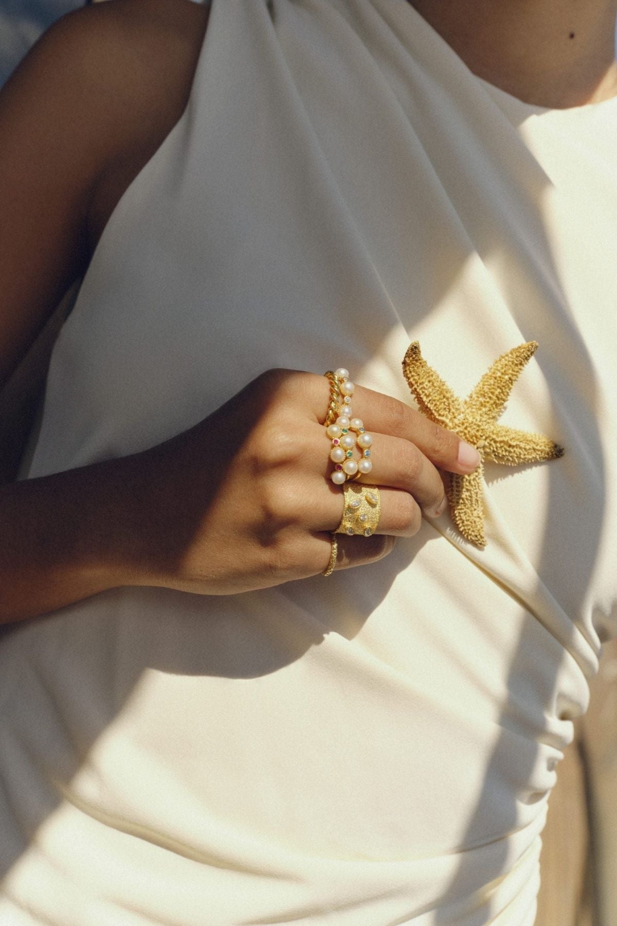 Close-up of a hand wearing gold rings with a white garment background