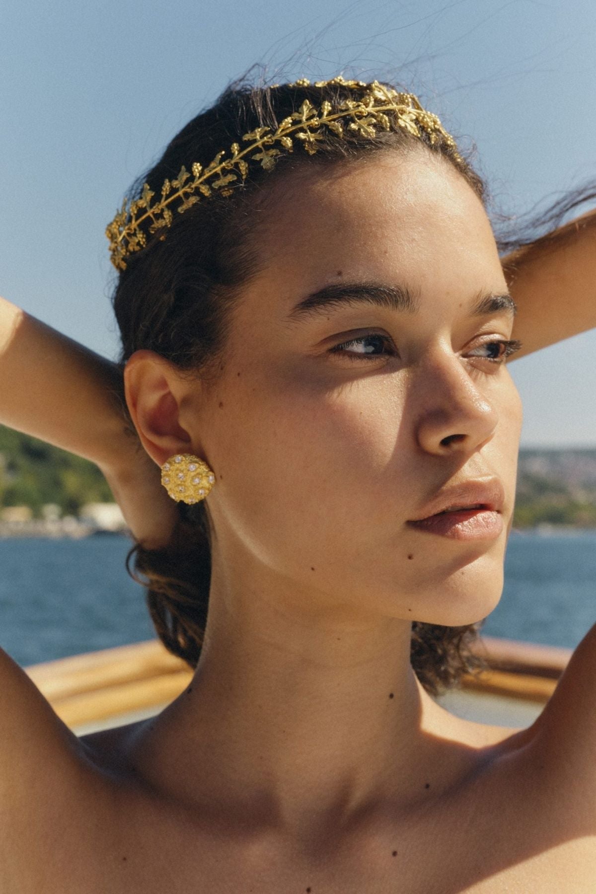 Woman wearing a gold headband and earrings with a scenic background