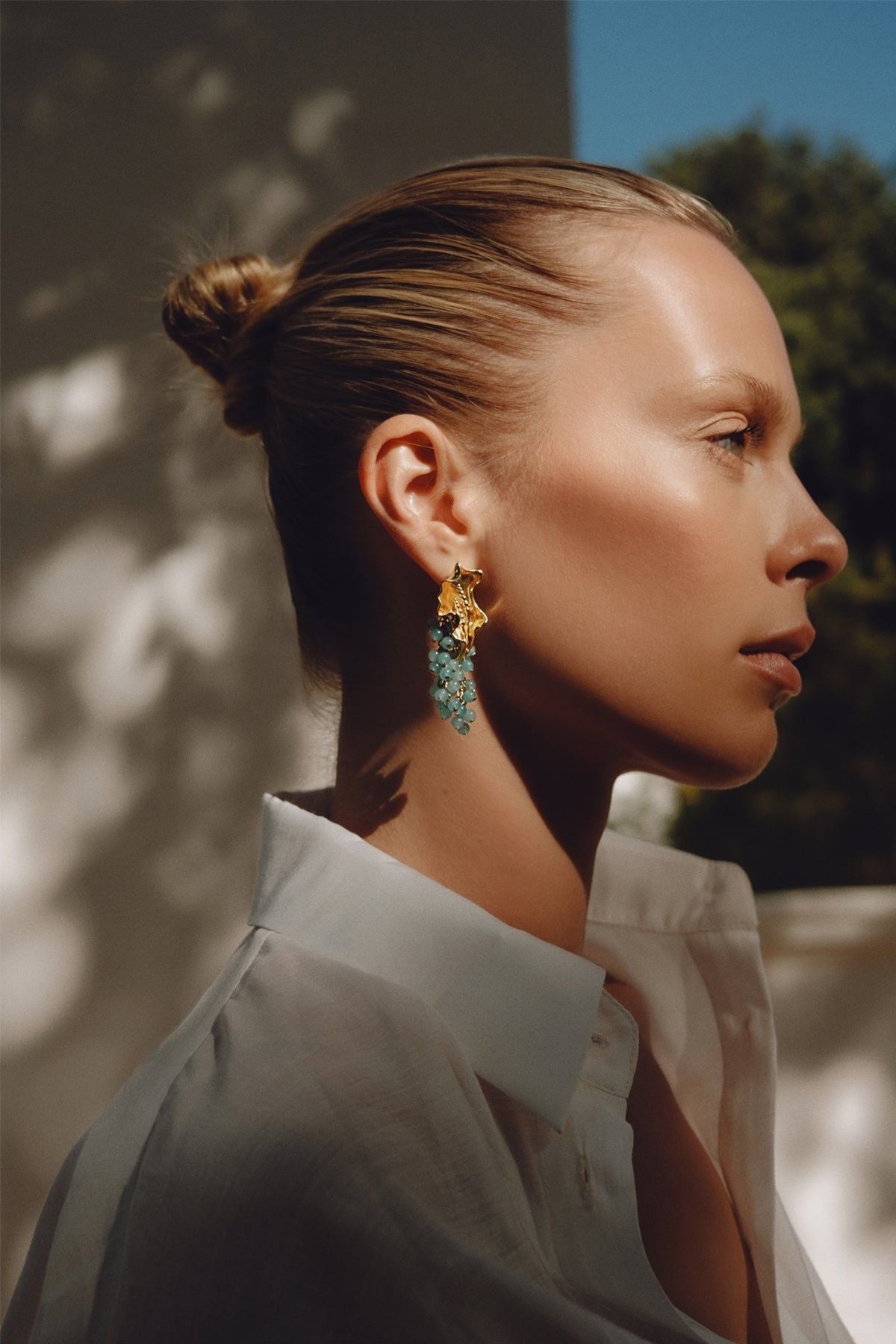 Woman wearing gold and green earrings with a blurred outdoor background
