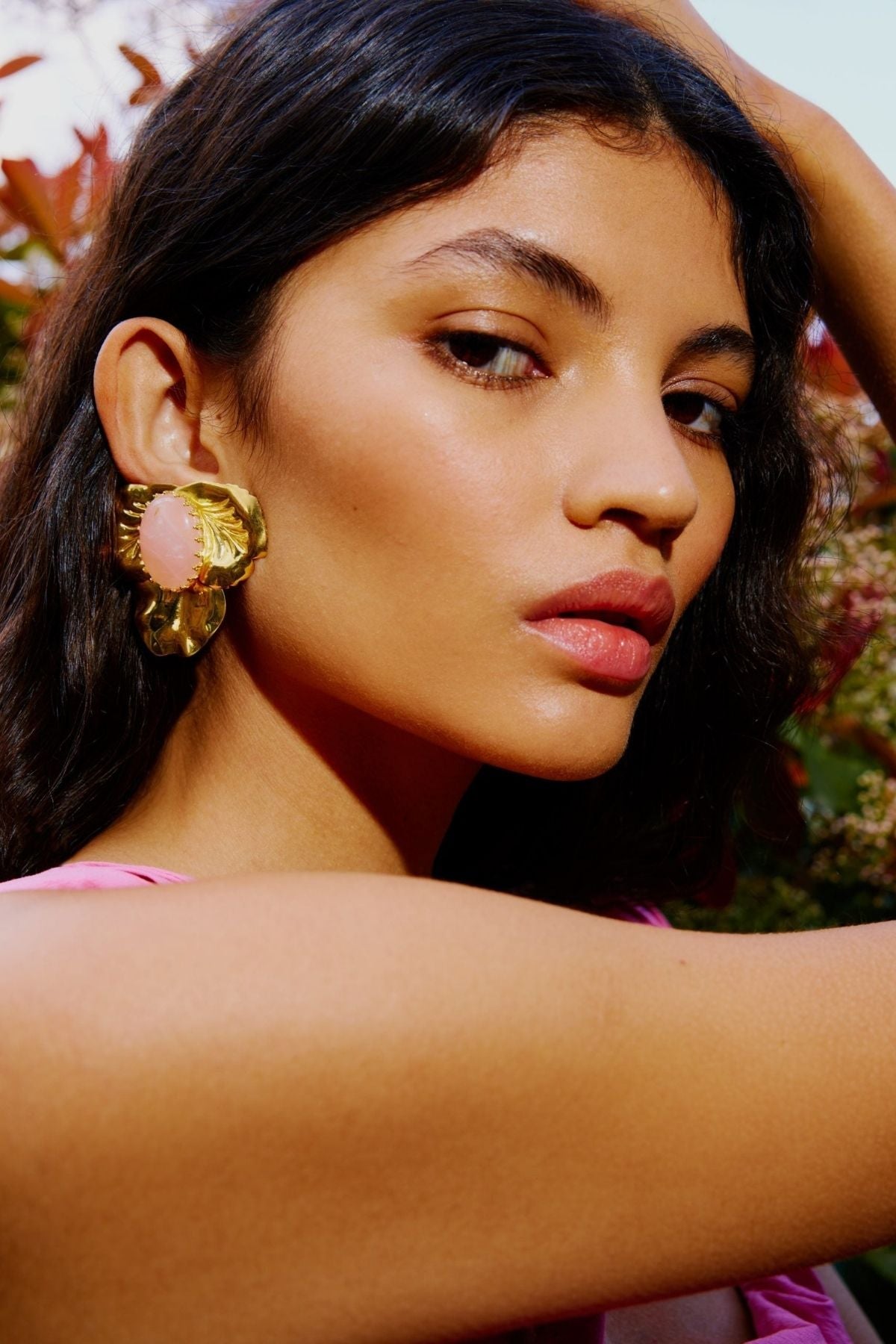 Close-up of a woman wearing large gold earrings with pink stones, outdoors.