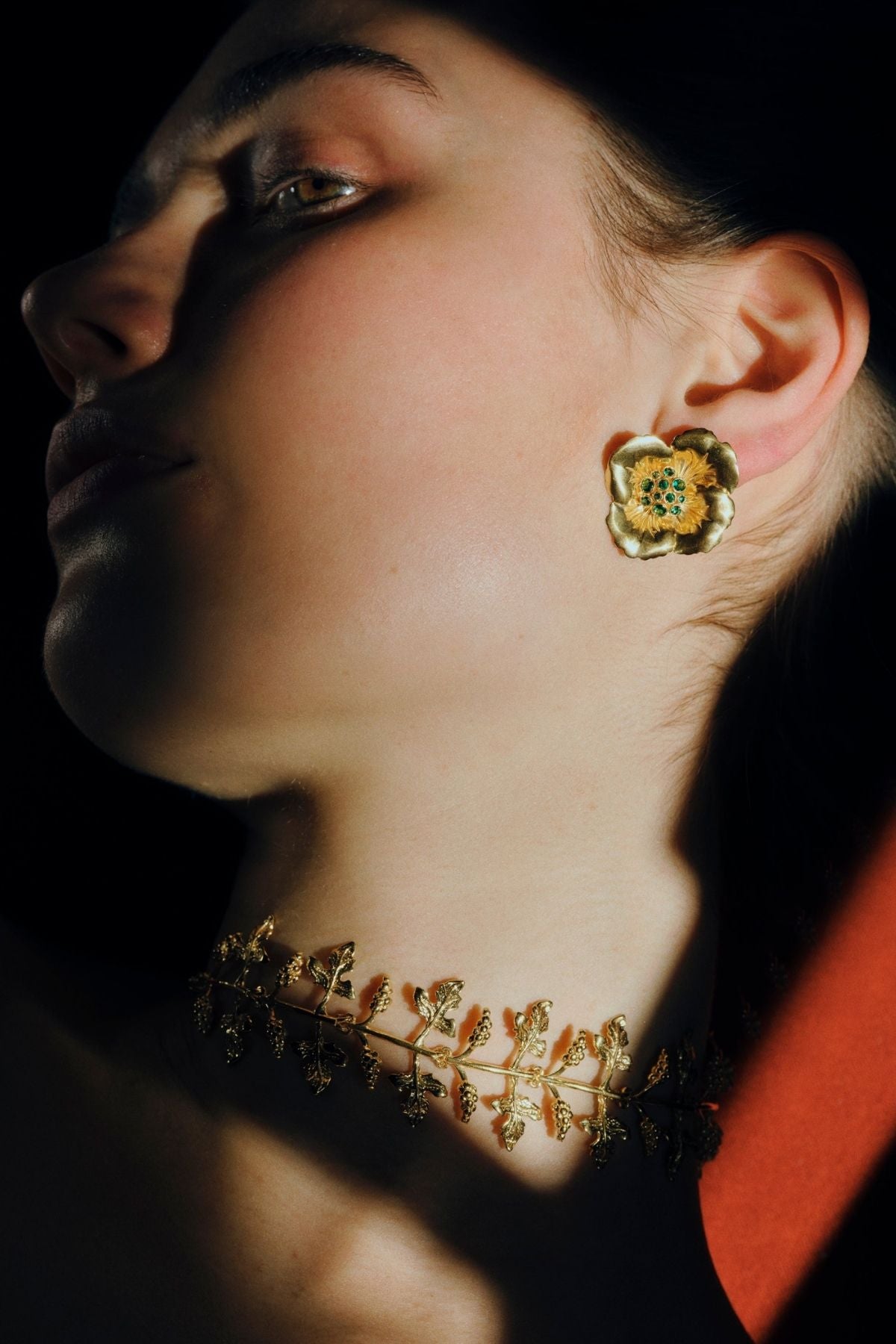 Close-up of a person wearing a floral earring and necklace against a dark background