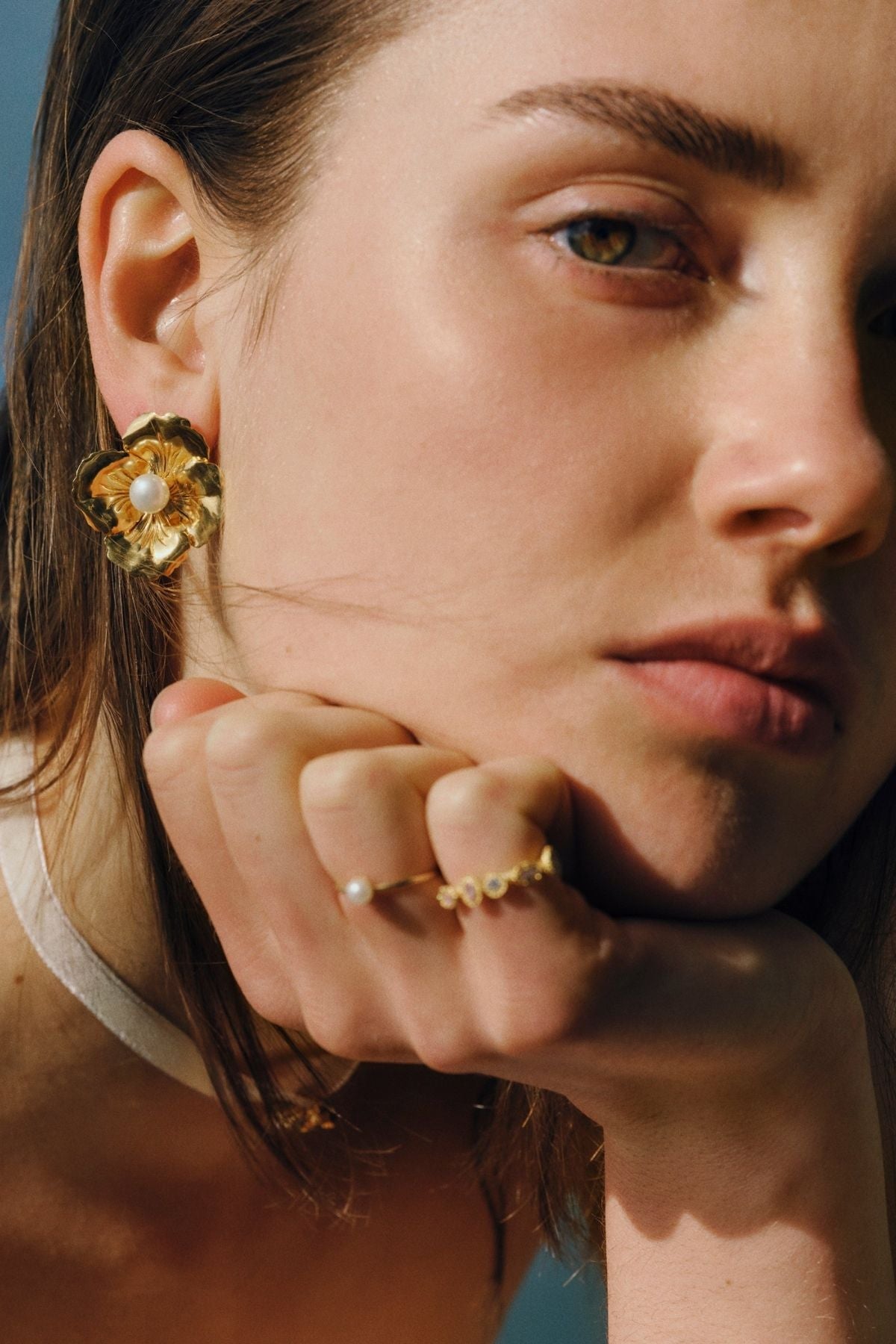 Close-up of a woman wearing gold earrings and a ring, with a blurred background.