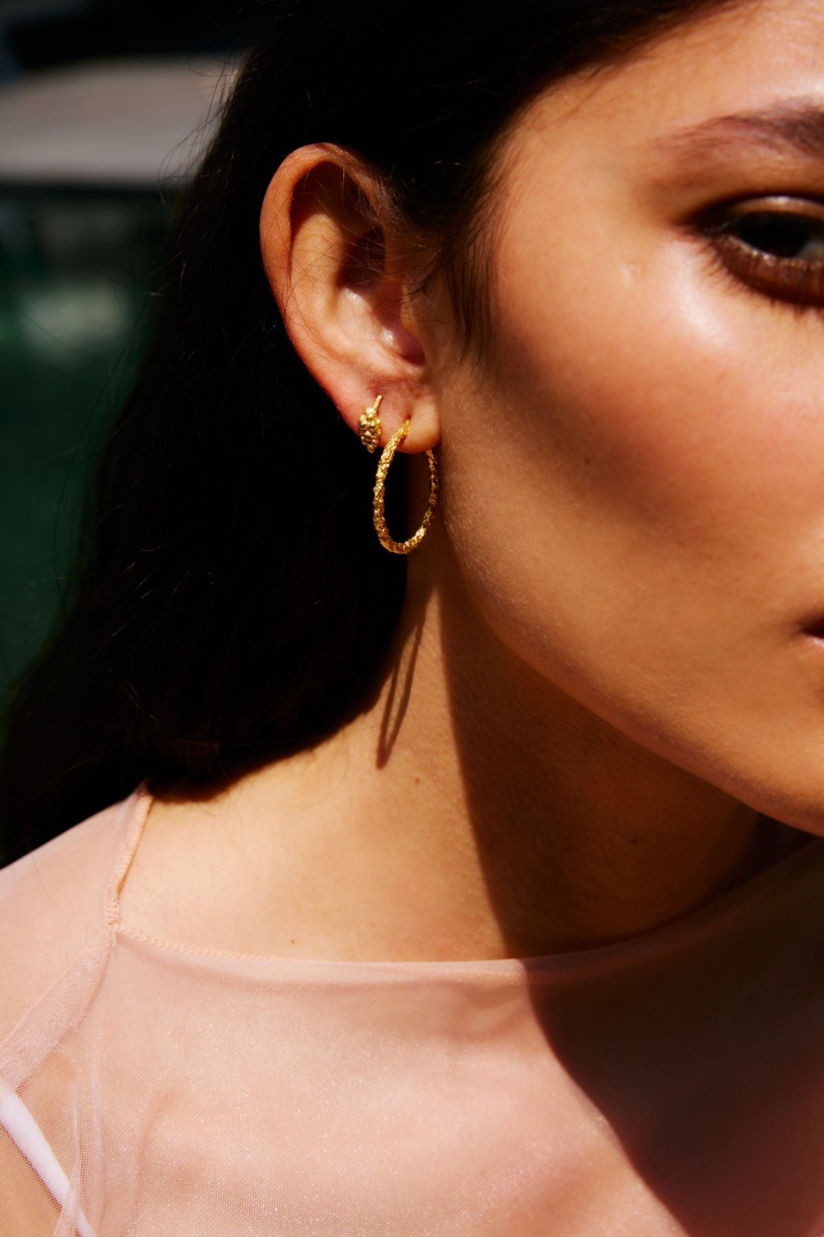 Close-up of a person wearing gold hoop earrings with a blurred background