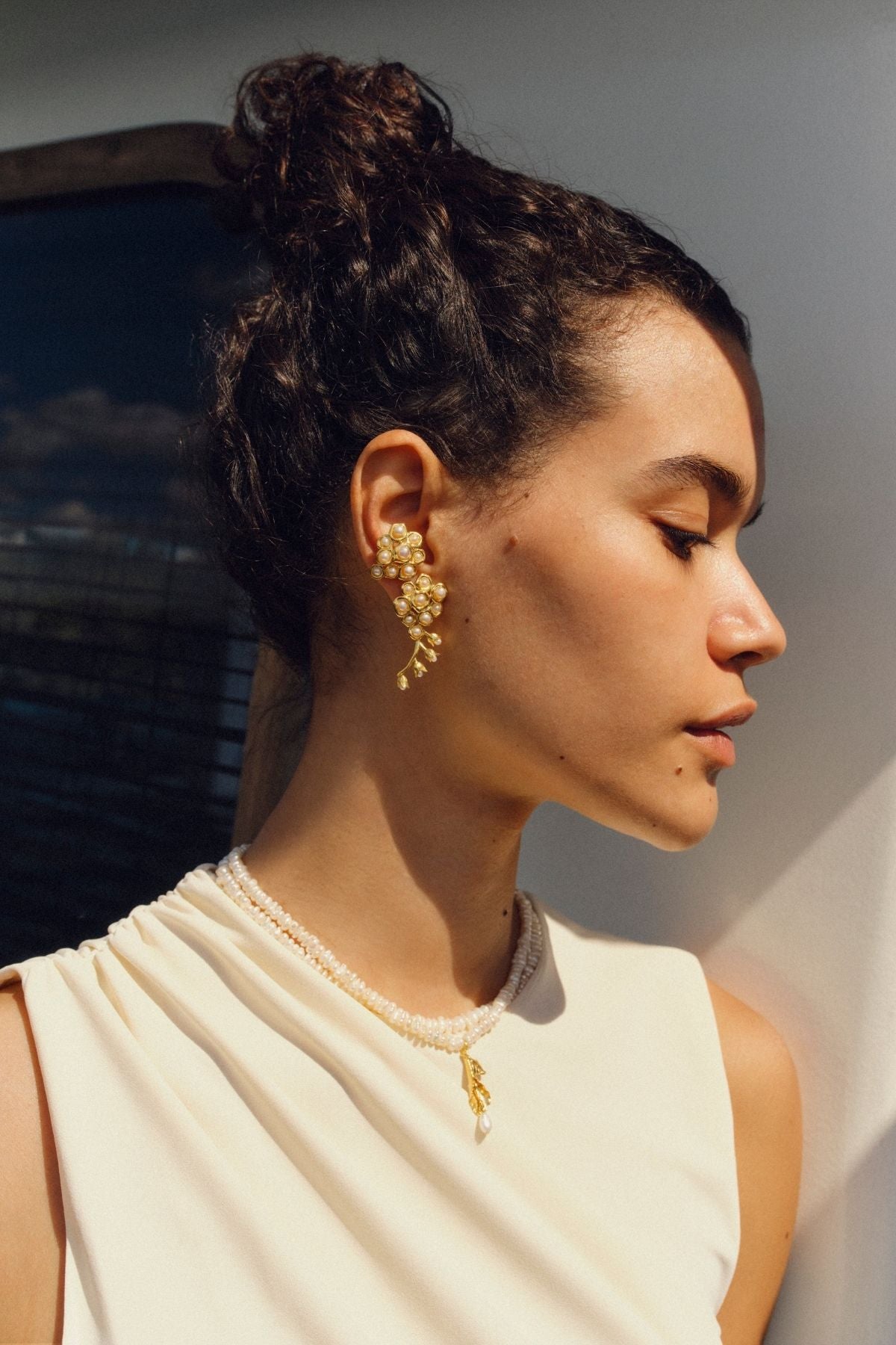 Woman wearing gold earrings and a necklace with a neutral background