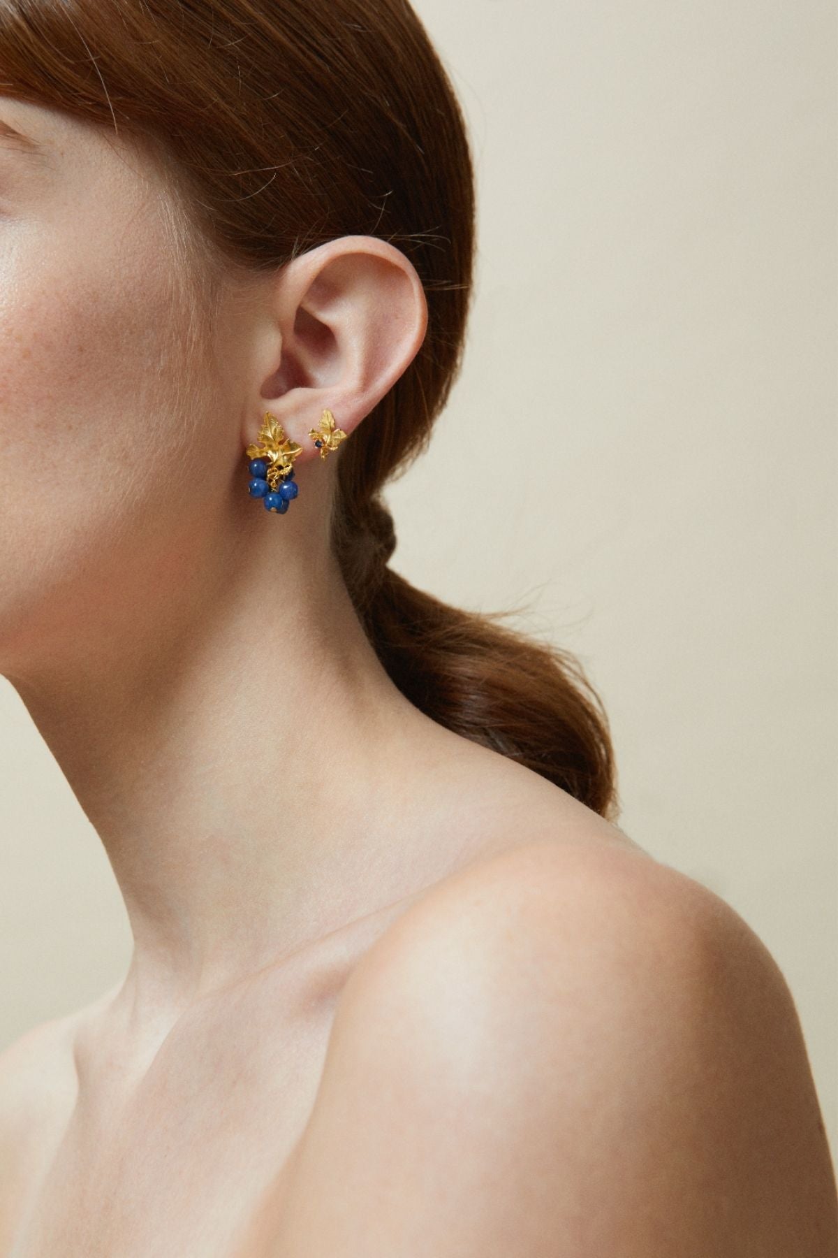 Close-up of a person wearing a pair of colorful earrings with a neutral background